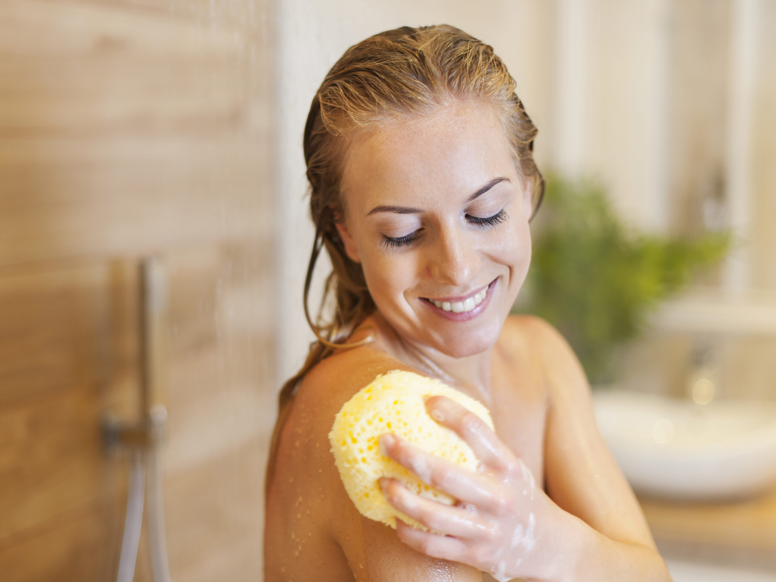 Freepik imagem: Mulher jovem tomando banho com bucha e sabonete líquido.