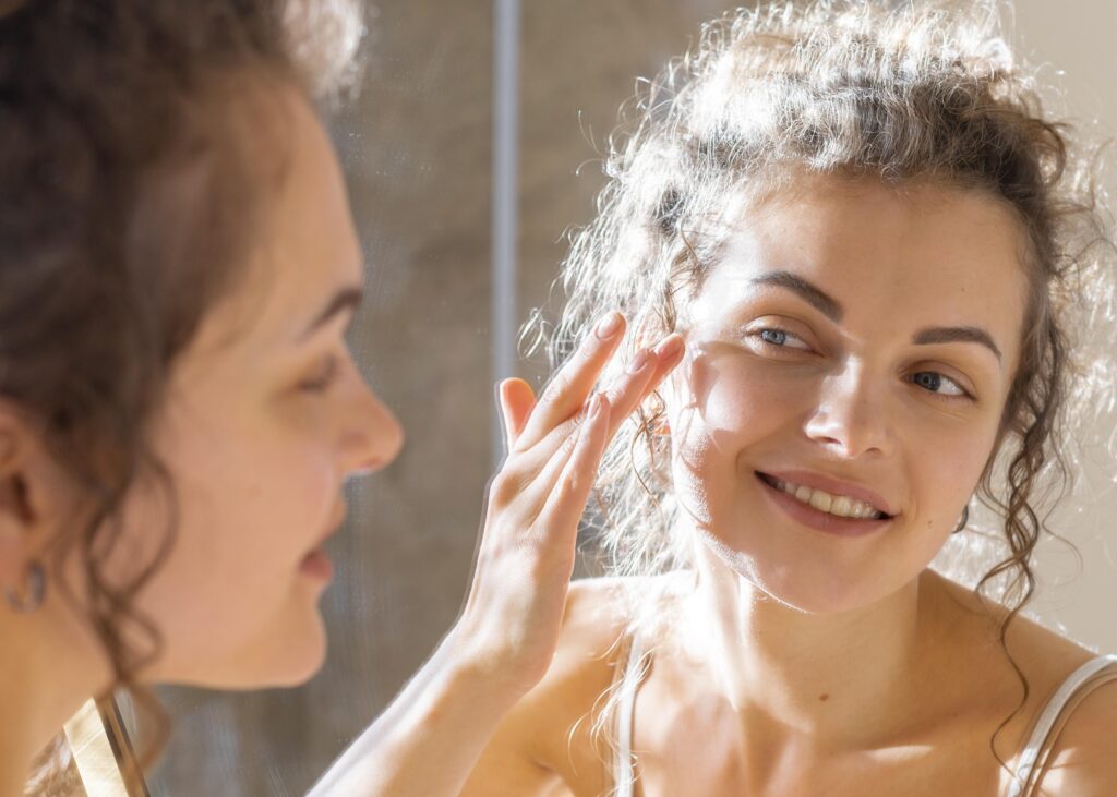 Freepik imagem: Mulher olhando no espelho e aplicando creme facial.
